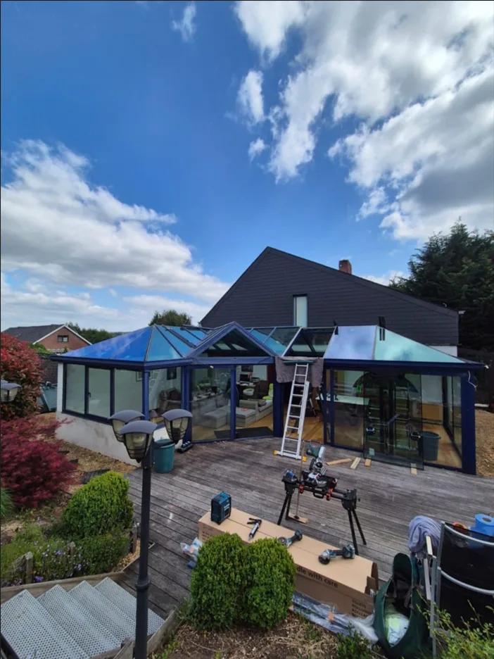 Chantier de véranda avec toiture vitrée, échelle et matériel sur la terrasse